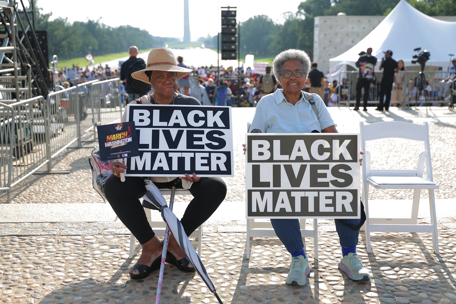 Two attendees seated holding Black Lives Matter signs, with the Washington Monument behind them.